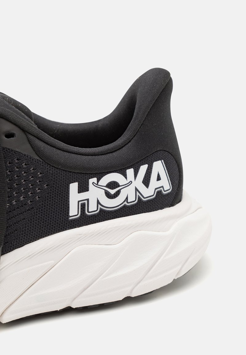 Scarpa sportiva nera con tomaia in rete, colletto imbottito, logo HOKA bianco e suola bianca testurizzata con distinti motivi di battistrada.