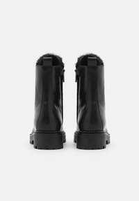 Stivaletti neri in pelle con suole chunky, interni foderati in pelliccia e chiusure con zip posteriori, mostrati da dietro su uno sfondo bianco.
