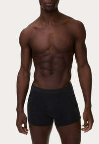 Schwarze Boxershorts mit einfarbigem Design und elastischem Bund, aus weichem Stoff, körperbetontem Schnitt und niedriger Taille. Hautfarbe ist sichtbar.