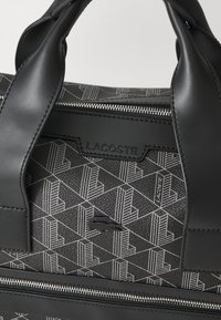 Black handbag with a geometric pattern in white, featuring a textured finish, leather handles, and a silver zipper closure.