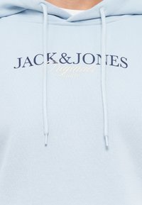 Hellblauer Hoodie aus weichem Stoff, mit einer Vorderseite Tasche, Kapuze mit Kordelzug und erhabenem Logo-Text in Marineblau und Creme.