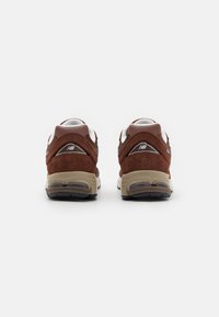 Smeđi sneakers od zamšika i mrežice s bijelim naglascima, s podstavljenim potplatom i vidljivom zračnom jedinicom na peti. Teksturirani stražnji panel s logotipom.