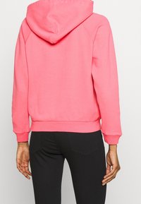 Rosa huvtröja i mjuk tyg, med raglanärmar och ribbad fåll. Bakifrån visas en avslappnad passform och huva.