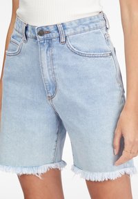 Shorts di denim azzurro chiaro con orlo sfilacciato. Design a cinque tasche, cuciture visibili e bottone in metallo in vita. Texture liscia.