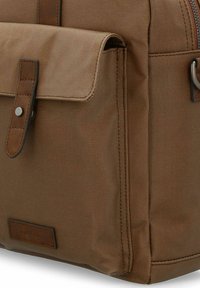 Brown canvas backpack featuring a front flap with a snap closure, leather accent, and visible stitching along the sides and edges.