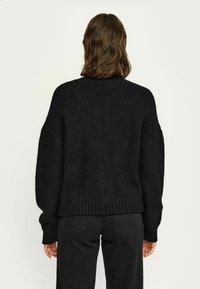 Schwarzer Strickpullover mit lockerer Passform, überschnittenen Schultern und geripptem Saum sowie Bündchen. Weicher Stoff, sichtbare Fasern und minimalistisches Design.