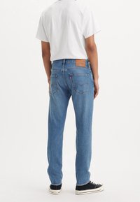 Světle modré džínové kalhoty mají rovný střih nohavic, viditelné švy a hnědou koženou záplatu na zadním pásu s logem značky.