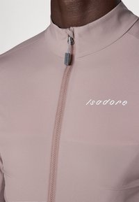 Maglia da ciclismo rosa chiaro con colletto alto, zip frontale completa e la scritta "Isadore" in bianco sul lato sinistro. Tessuto morbido e elastico.