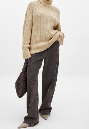 Beige chunky strikket rullekravesweater kombineret med mørke vidde bukser, beige spidse sko og en mørk vævet håndtaske.