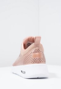 Rosa Nike-sneakers med ventilerad häl och vit sula, sedd från baksidan på en vit yta och bakgrund.