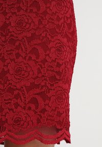 Tissu en dentelle rouge avec un motif floral détaillé et un ourlet festonné sur un vêtement.