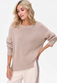 Jasno beżowy sweter wykonany dzianiny z prążkowanym wykończeniem i rękawami zakończonymi mankietami. Luźny krój oraz okrągły dekolt. Miękka tekstura i swobodny design.