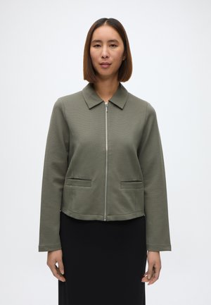 Olajzöld, rövid fazonú dzseki gallérral, cipzáras záródással és két elülső zsebbel; texturált anyag, sima felülettel.