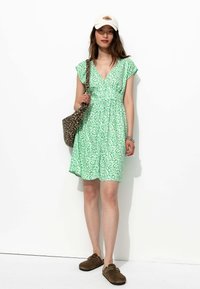 Robe florale verte avec des manches courtes évasées, décolleté en V et élastique à la taille. Assortie à un sac à imprimé léopard et des chaussures slip-on brunes.