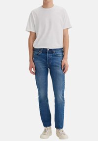 Camiseta blanca de manga corta, jeans de mezclilla azul y zapatillas beige. Los jeans tienen un corte recto clásico, una textura suave y detalles de costura sutiles.