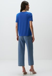 Niebieska koszulka z krótkim rękawem z gładkiego materiału, w zestawie z jasnoniebieskimi spodniami dzwonami. Ubranie cechuje luźny krój i minimalistyczny design.
