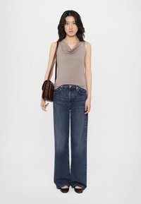 Beige ermeløs topp med drapert halslinning, sammen med brede blå denimbukser. Svart sko og en brun skulderveske fullfører antrekket.