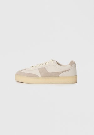 Beige and gray suede sneaker with a textured surface, lace-up design, and a thick cream sole. Features contrasting panels and stitching.