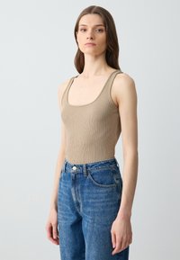 Beige geribbelde tanktop met brede schouderbanden, gedragen met hoge blauwe denim jeans. De top heeft een ronde halslijn en een aansluitend ontwerp.