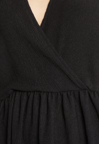 Vestido negro con una tela texturizada, que presenta un escote en V profundo y una cintura fruncida, creando una silueta suave y fluida.