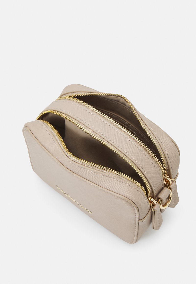 Borsa in pelle beige con doppie chiusure a zip dorate, forma arrotondata e logo in rilievo sulla parte anteriore; texture liscia con design minimalista.