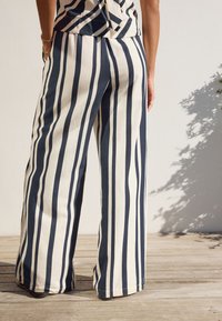 Striped wide-leg trousers in navy and cream fabric, featuring vertical stripes, a loose fit, and a hem that brushes against the floor.