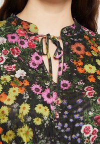 Robe florale avec un fond noir, mettant en avant des couleurs vives comme des fleurs roses, jaunes et orange. Elle possède un col en goutte d'eau avec une fermeture à nouer.