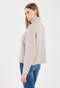 Pulover bej cu guler înalt, cu un croi relaxat, având mâneci lungi și o lungime scurtă, asortat cu blugi din denim albastru.