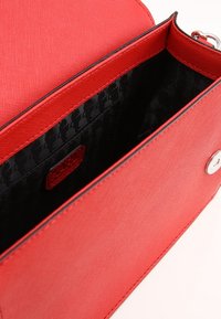 Borsa a spalla sintetica rossa con esterno testurizzato, munita di una fodera interna con un design nero a pattern e una chiusura a bottone argentato.