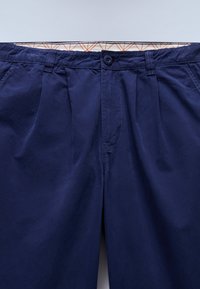 Παντελόνι σε ναυτικό μπλε με λεία υφή, διαθέτει κλείσιμο με κουμπί και πιέτες μπροστά. Η εσωτερική ζώνη μέσης έχει γεωμετρικό σχέδιο.