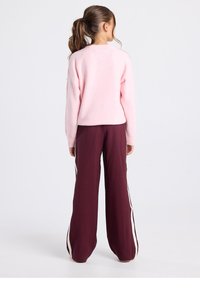 Hellrosa flauschiger Pullover mit langen Ärmeln, kombiniert mit lockeren burgunderroten Hosen mit weißen Seitenstreifen. Einfacher, entspannter Schnitt.