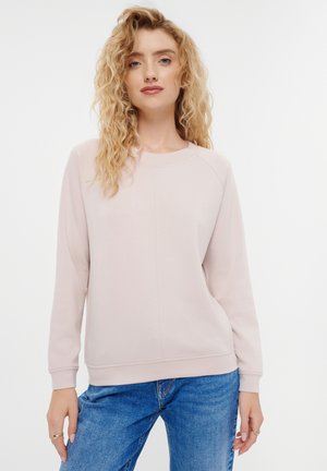 Felpa rosa chiaro con scollo rotondo, maniche raglan e un pannello frontale testurizzato. Abbinata a jeans in denim blu. Tessuto morbido.