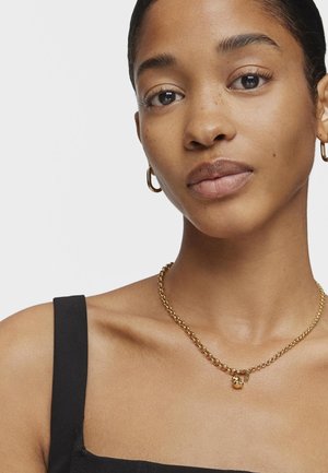 Collana in oro con anelli tondi, con un piccolo ciondolo a forma di lucchetto e chiusura regolabile, indossata sopra una maglia nera.