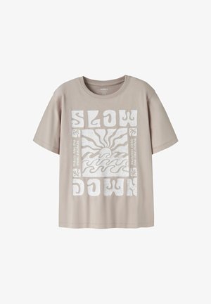 Beige kortærmet t-shirt med hvid grafik af solnedgang over bølger, stiliserede bogstaver der staver "SLOW DOWN" og små palmeikoner.