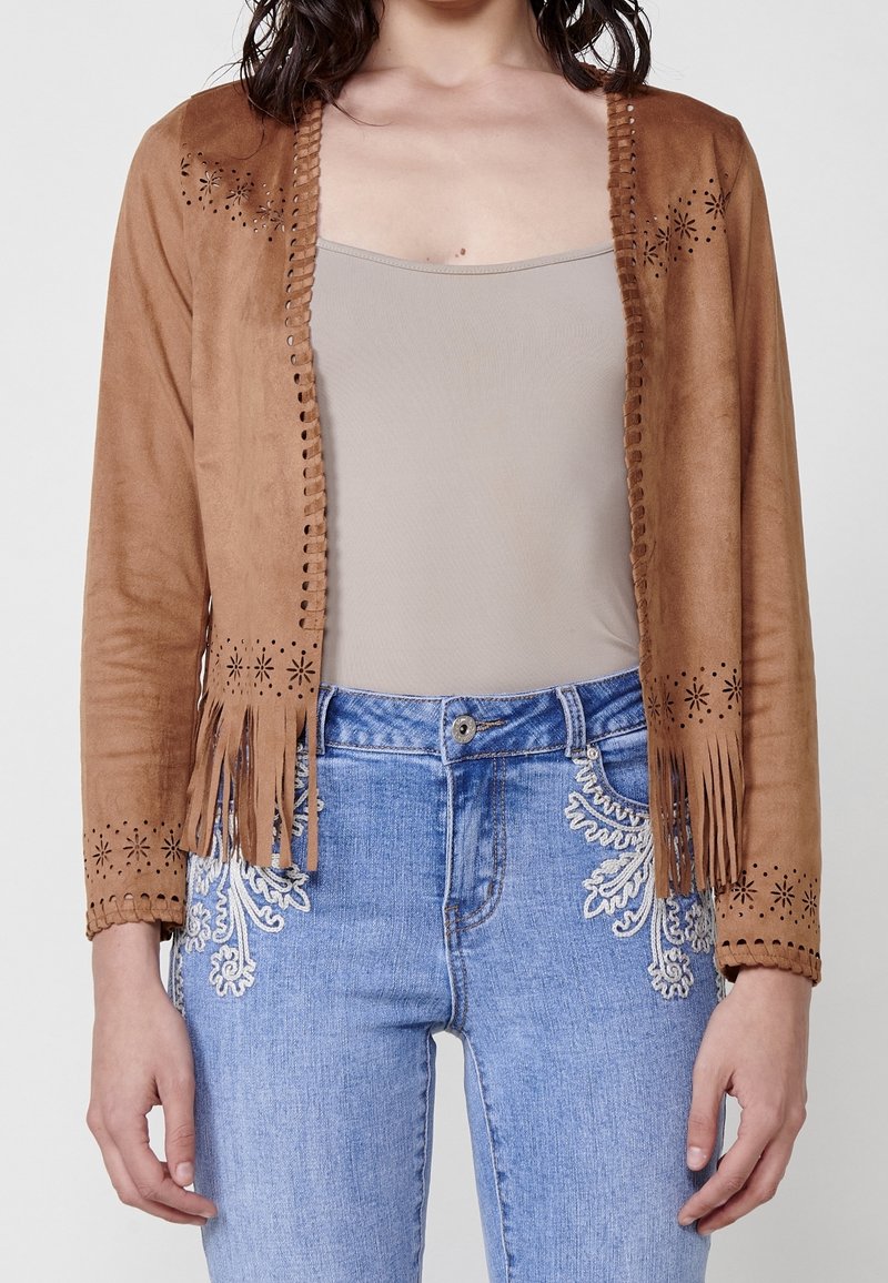 Femme portant une veste en suède beige à franges avec des motifs d'étoiles découpés au laser, sur un débardeur beige et un jean bleu avec broderies blanches.