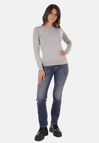 Maglietta a maniche lunghe grigio chiaro, realizzata in materiale morbido, abbinata a jeans blu in denim e stivali neri chunky con lacci. Design semplice, forma aderente.