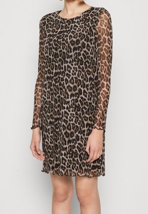 Femme portant une robe léopard mi-longue à manches longues avec des manches transparentes et un col rond, debout devant un fond uni.