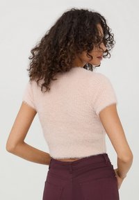 Maglione corto di un rosa chiaro, con maniche corte e un tessuto testurizzato e morbido. Abbinato a pantaloni di un burgundy scuro, con un orlo delicato.