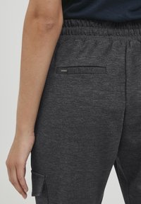 Grå, texturerade joggers med elastisk midja och en liten bakficka med en svart metalltag. Enkel, funktionell design.