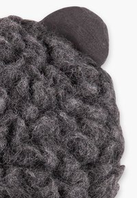 Accessoire en peluche gris en forme d'ours avec des cheveux texturés et bouclés et un détail d'oreille lisse et arrondi. Le tissu doux crée une surface tactile.