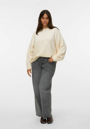 Light cream oversized sweater with dropped shoulders, ribbed cuffs, paired with high-waisted grey jeans and brown footwear.