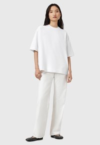 Witte oversized crewneck t-shirt, gecombineerd met losse witte broek. Zwarte instappers met witte stippen. Eenvoudige, casual uitstraling.