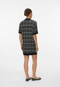 Robe courte à carreaux noir et blanc avec des manches courtes, tissu texturé, col rond et silhouette légèrement cintrée. Chaussures noires plates incluses.