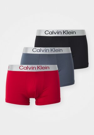 Trīs pāri Calvin Klein bokseru apakšveļas sarkanā, pelēkā un melnā krāsā. Katram ir mīksts elastīgs josts ar logotipu.