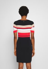 Robe en tricot avec des rayures horizontales rouge, noir, or et blanc. Manches courtes, silhouette ajustée et texture côtelée en haut.