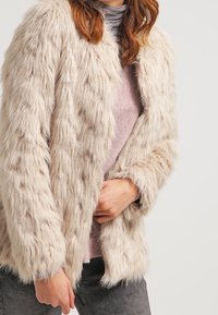 Faux pälsjacka i ljusbeige med en plyschig, texturerad yta. Öppen frontdesign med långa ärmar och en mjuk, mysig foder.