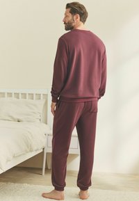 Bordó loungewear szett, amely egy kerek nyakú, hosszú ujjú felsőből és a hozzá illő, rugalmas mandzsettával ellátott nadrágból áll, texturált anyagból készült.