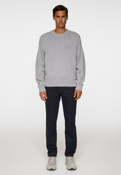 Gray sweater with ribbed cuffs and hem, relaxed fit, and plain texture; paired with dark navy pants and gray sneakers.