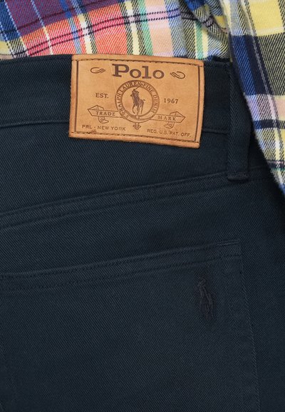 Kožená nálepka Polo Ralph Lauren na tmavomodrých džínsach, v kombinácii s farebnou károvanou košou.