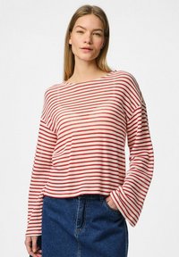 Maglione a righe rosse e bianche con maniche lunghe e scollatura ampia, abbinato a una gonna di jeans. Tessuto a maglia testurizzato e vestibilità comoda.